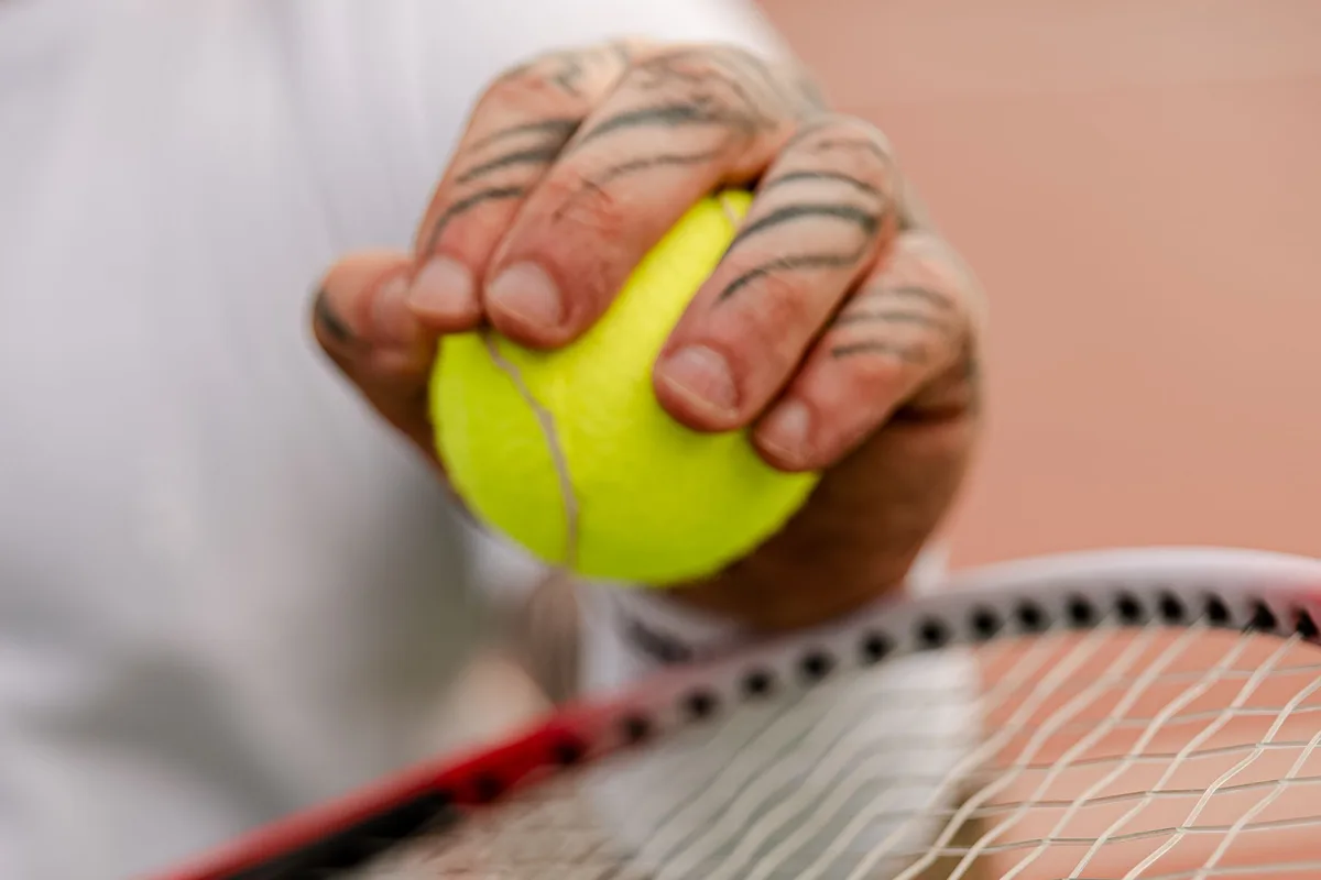 Tenis raketinin telleri üzerinde top tutan oyuncunun eli