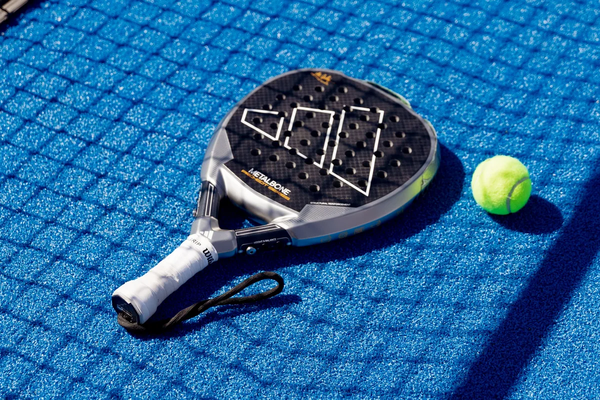 Mavi kortta delikli padel raketinin yanında duran sarı top