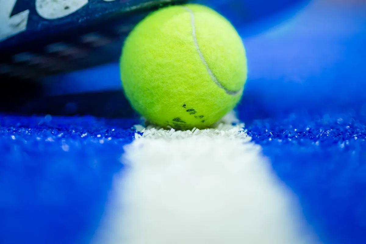 Mavi kortta padel raketinin kenarı ve sarı top