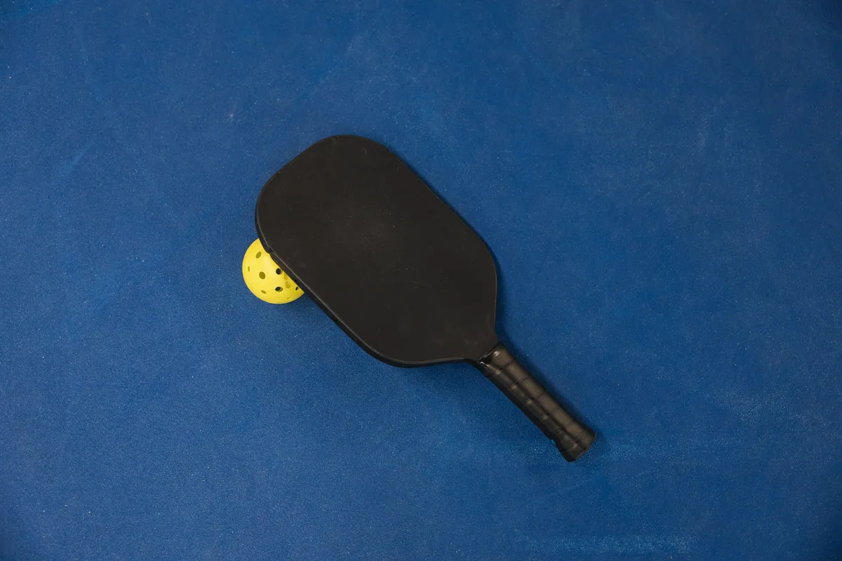 Mavi kortta siyah pickleball raketi ve sarı top