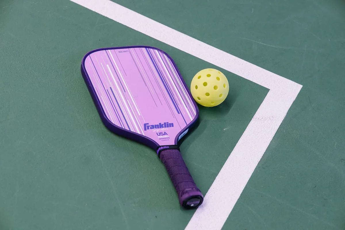 Sarı topun yanında sapı sarılı mor pickleball raketi