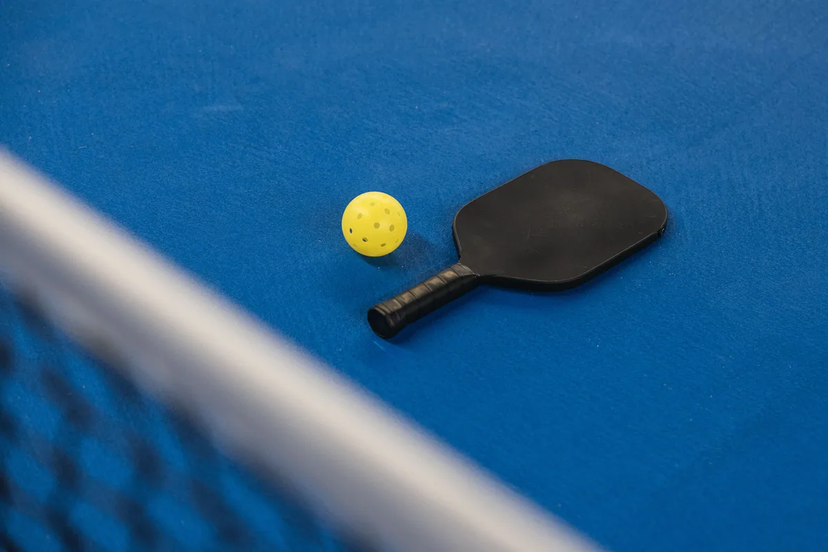 Pala de pickleball y pelota perforada junto a la red